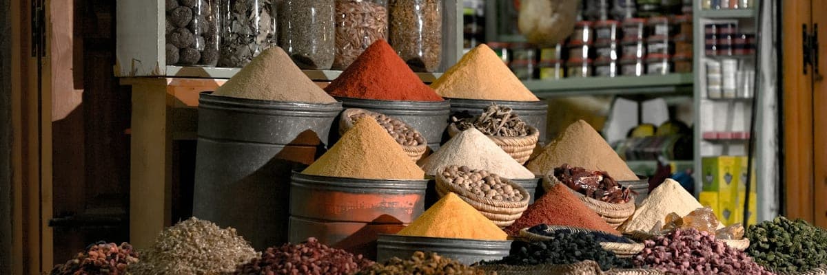 Een kruidenwinkel met piramides van gekleurde specerijen en potten met gedroogde kruiden op de planken erachter.